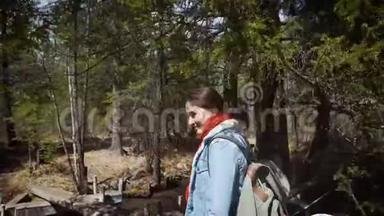 快乐的女孩旅行者穿过野生森林。 穿着牛仔裤，徒步旅行夹克和徒步旅行背包。 一片茂密的森林